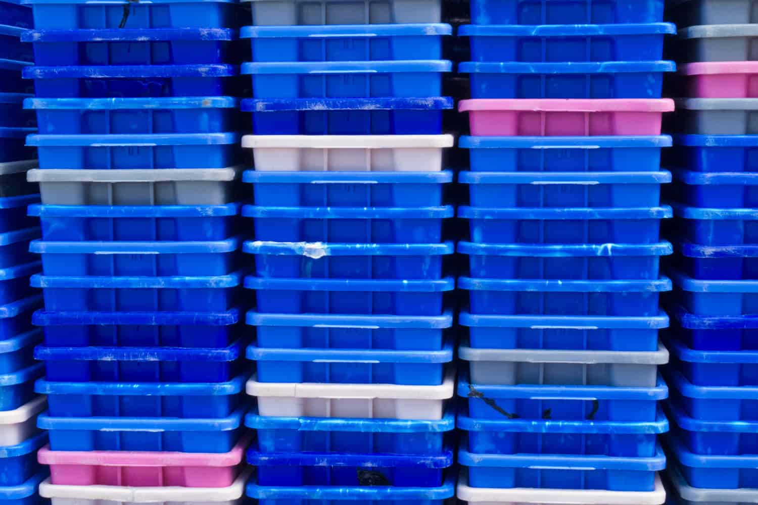 Background texture pattern of stacks of empty colorful plastic containers as used in fishery, wholesale, storage of fresh produce, cargo and retail transportation