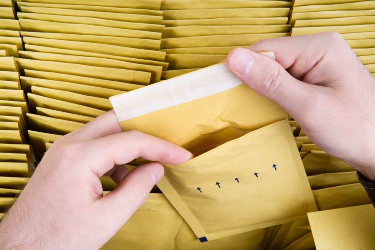 Self sealed mailing envelope quality inspection. Male hands open one yellow bubble mailer out of a bunch of shipping airmail packets.