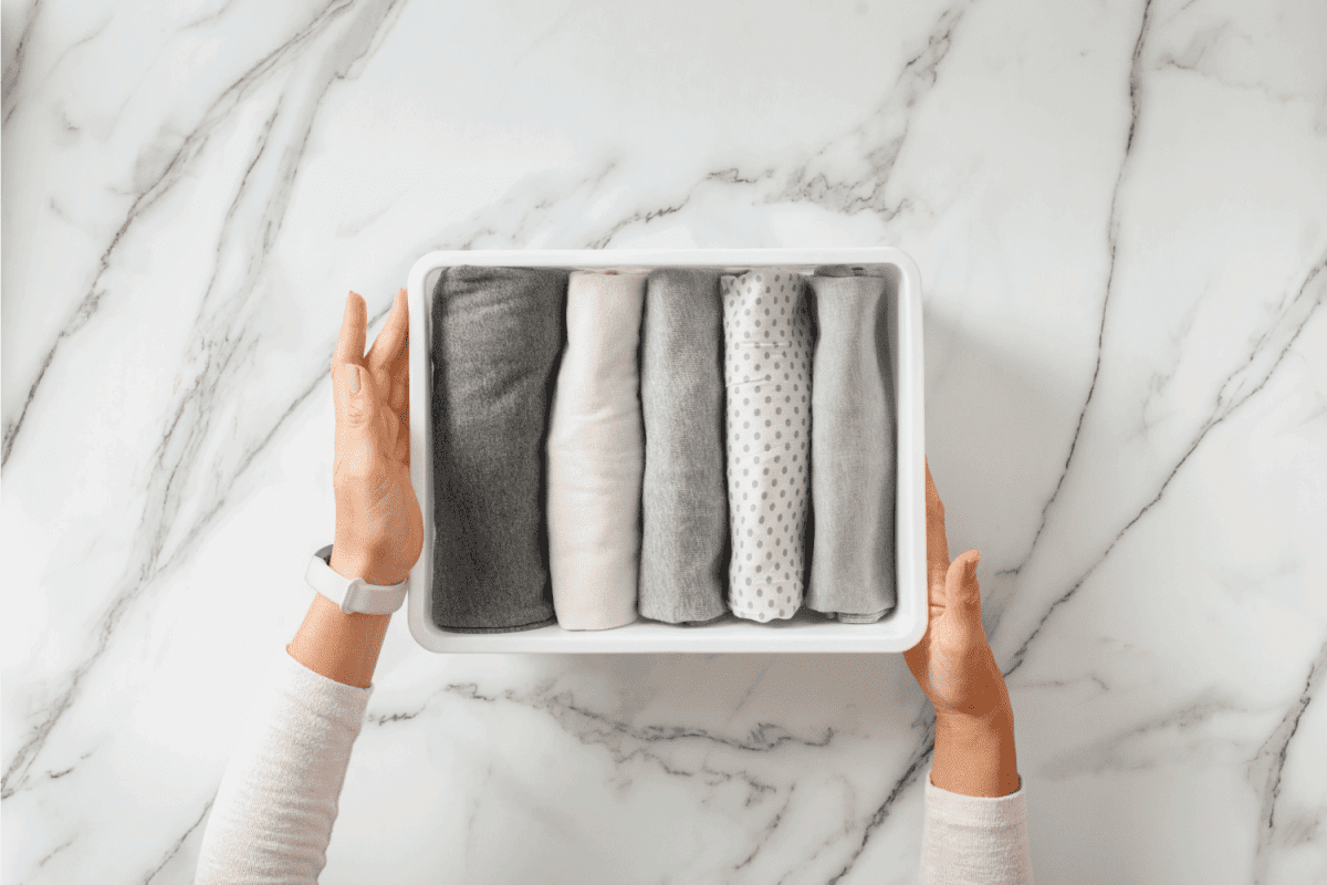 Woman hands neatly folding underwears and sorting in drawer organizers on white marble
