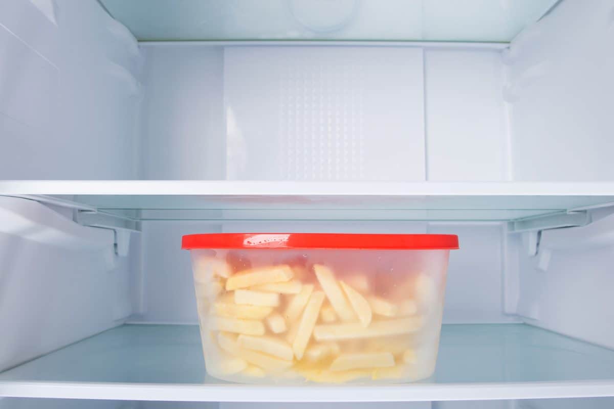 french fries in a plastic container, standing on the shelf of the refrigerator, on a white background
