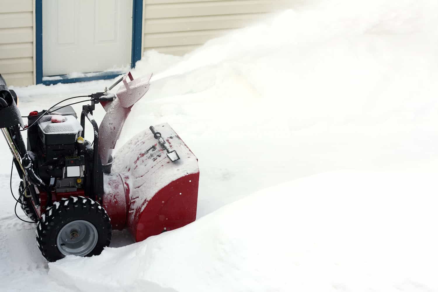 A photograph of a snow blower in action outside a home.