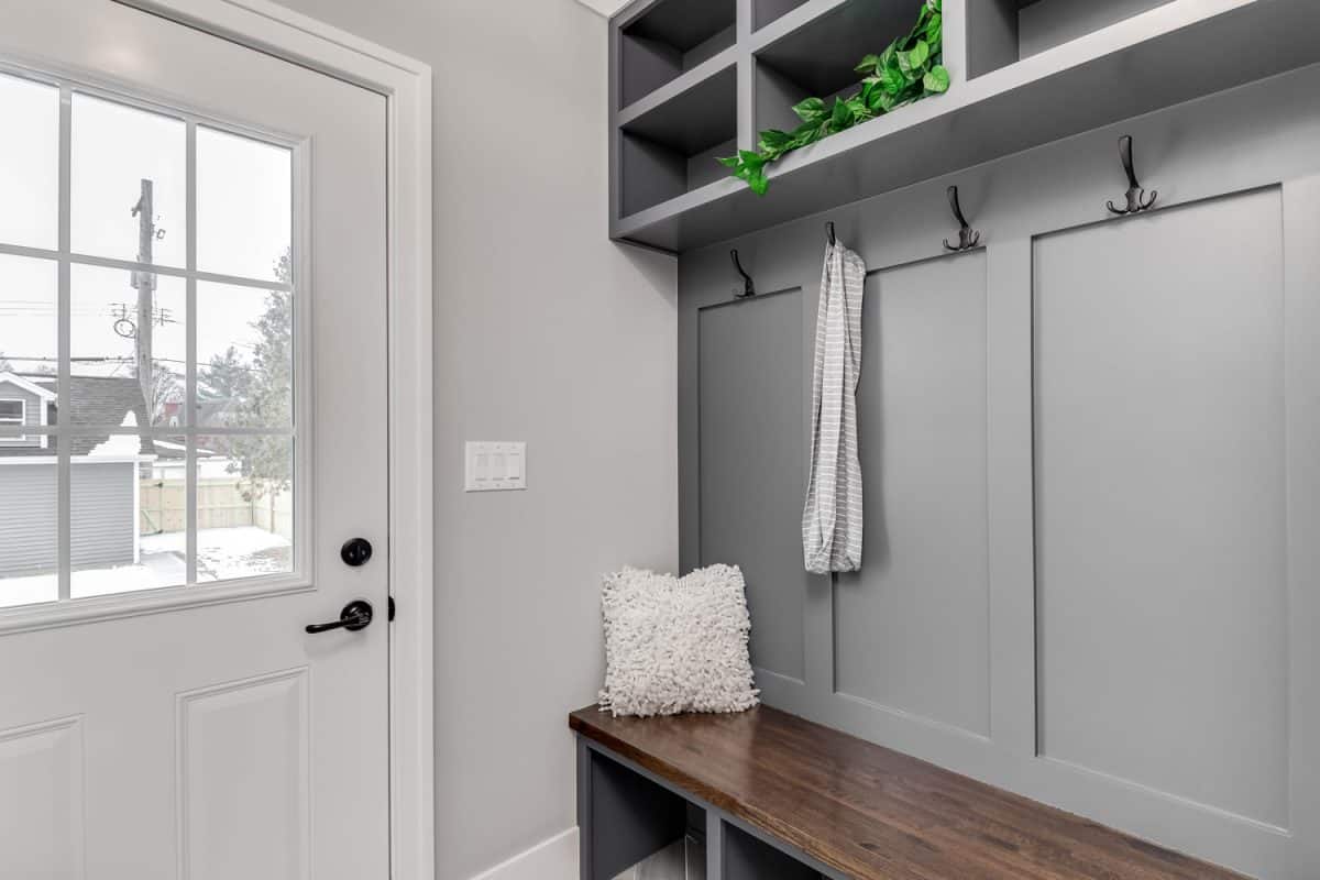 A staged detail shot of a gray mudroom / entryway with bench seating, coat hooks, and storage above. 