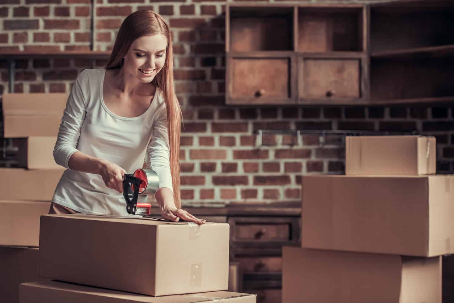 Beautiful young woman is packing cardboard boxes and smiling while moving into new apartment