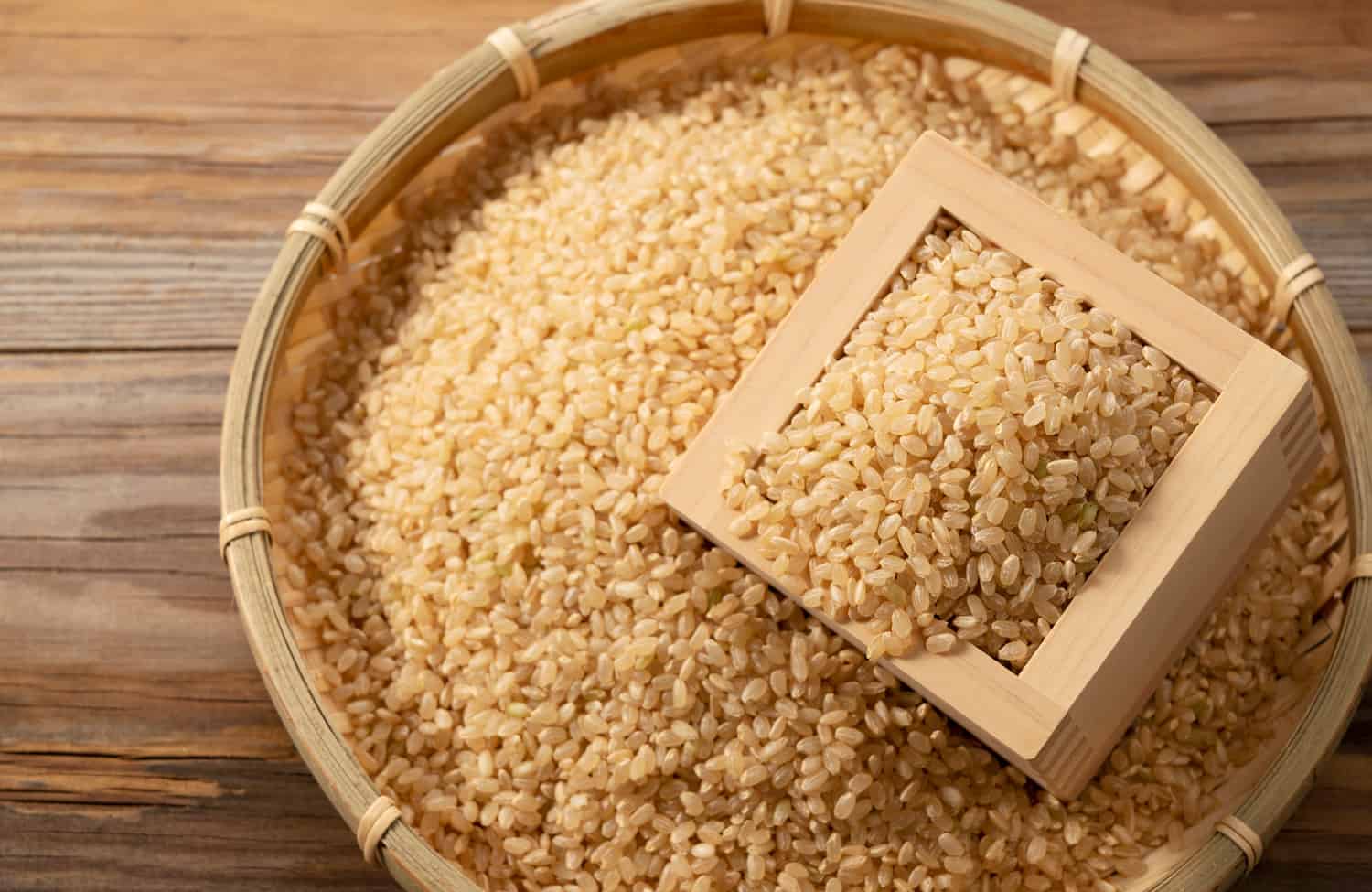 Brown rice in a wooden box and bamboo colander placed on a wooden background.