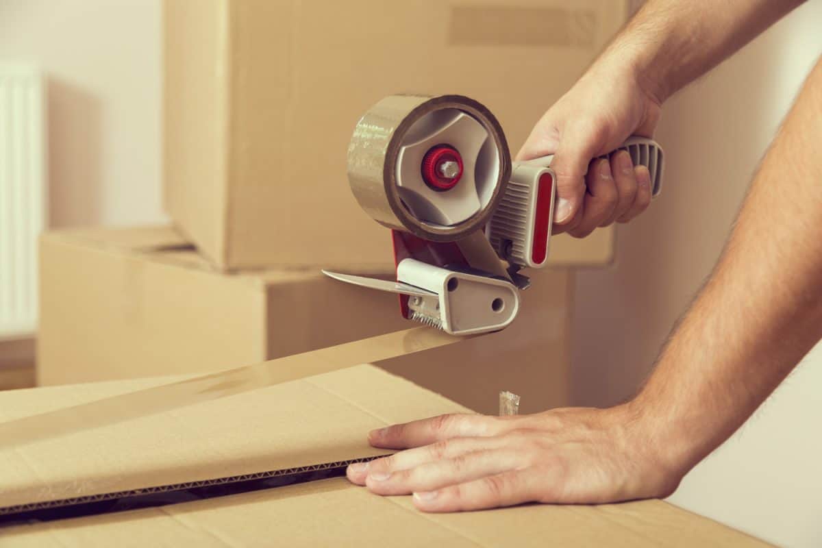 Close up of a guy's hands holding packing machine and sealing cardboard boxes with duct tape

