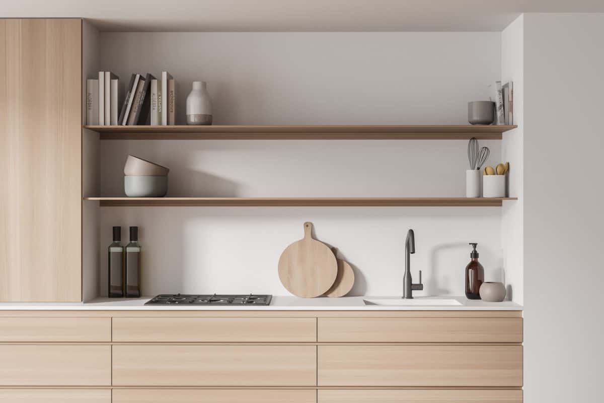 Close-up view of the kitchen interior with cabinet, having open shelves, wooden drawers of different sizes, white worktop and walls. 