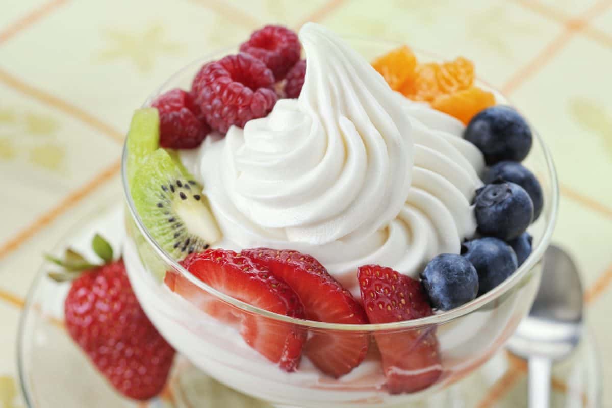  DIsh of vanilla soft-serve frozen yogurt surrounded by a variety of fresh fruits.