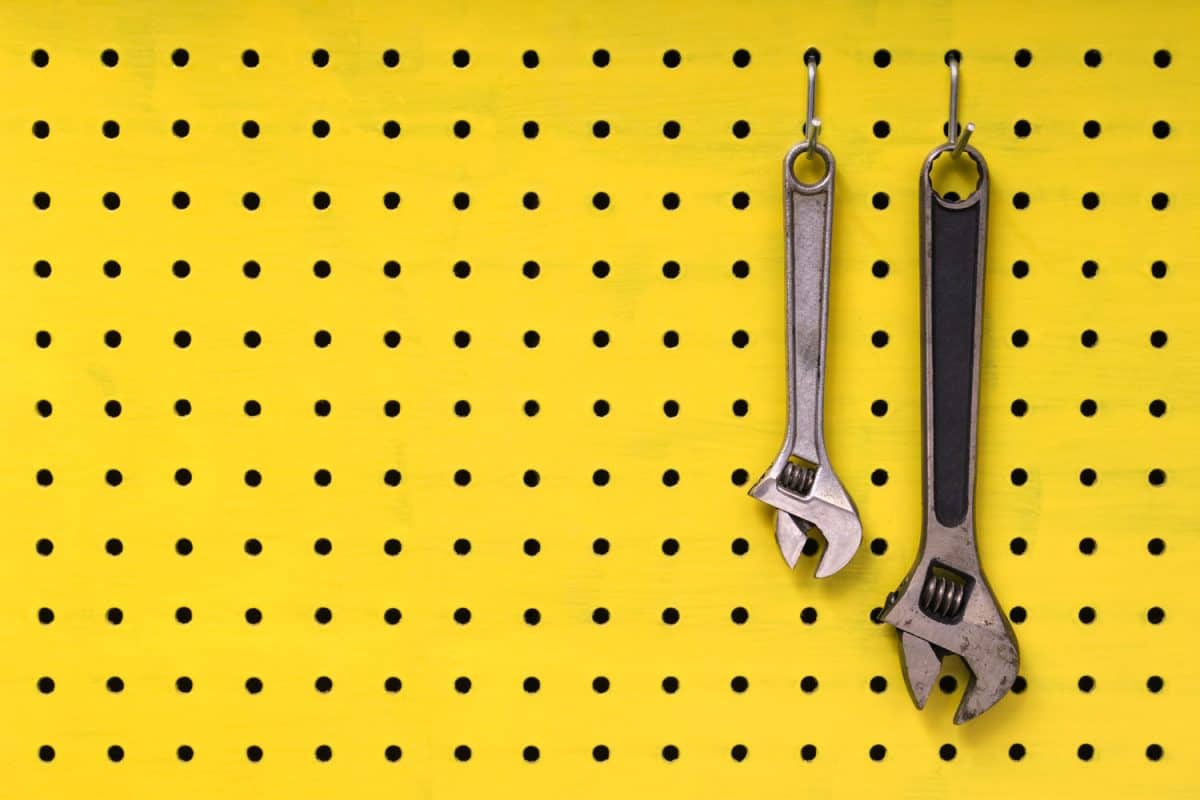 Pair of metal wrenches hang together off of hooks on yellow pegboard.