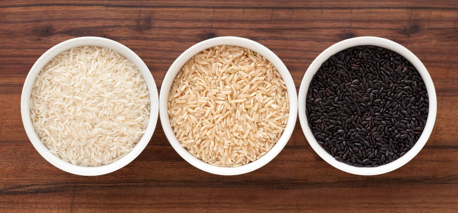 Top view of three bowls containing rice varieties (basmati, brown and black)
