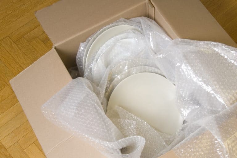 White plates wrapped in bubble wrap stacked in a moving box
