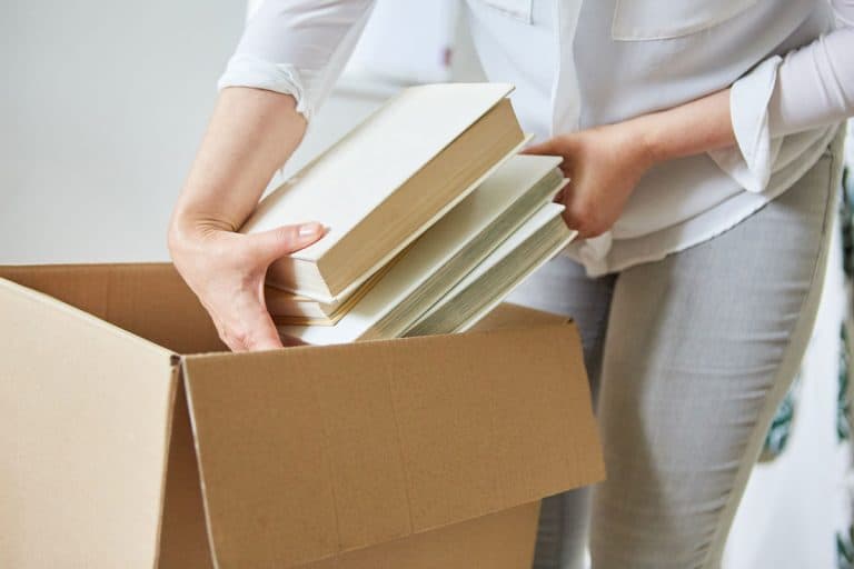 Woman packs books in a moving box for moving to the new house, Should You Store Books In Cardboard Or Plastic Boxes?