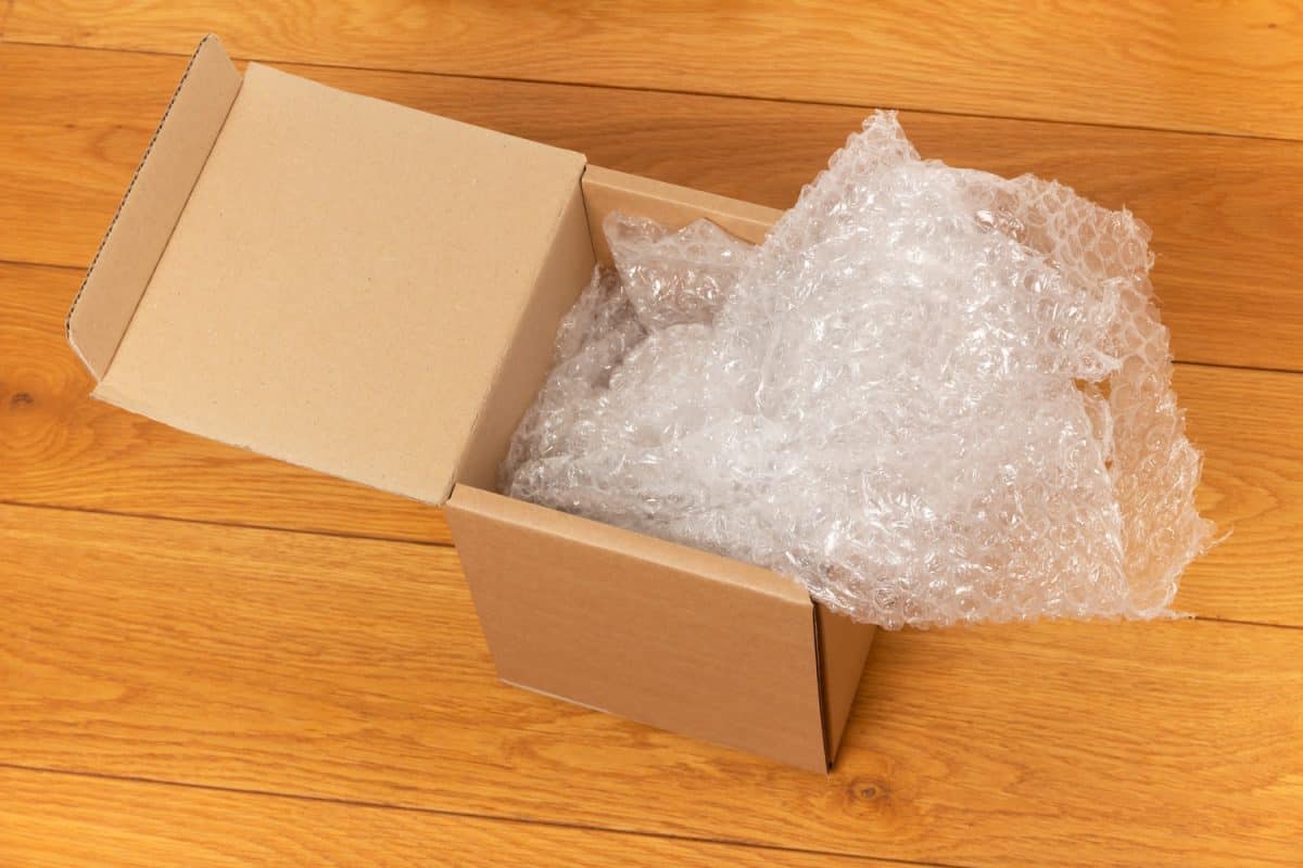 open cardboard box with bubble wrap on the wooden floor of the room

