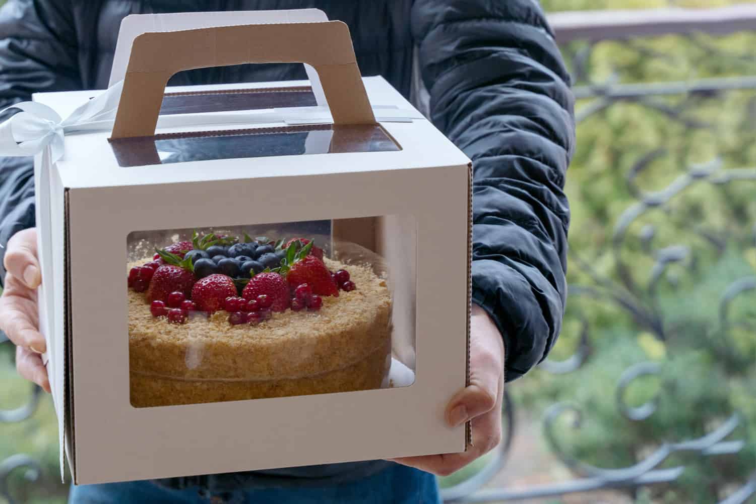 uman hands holding cardboard box with holiday cake decorated of berries. 